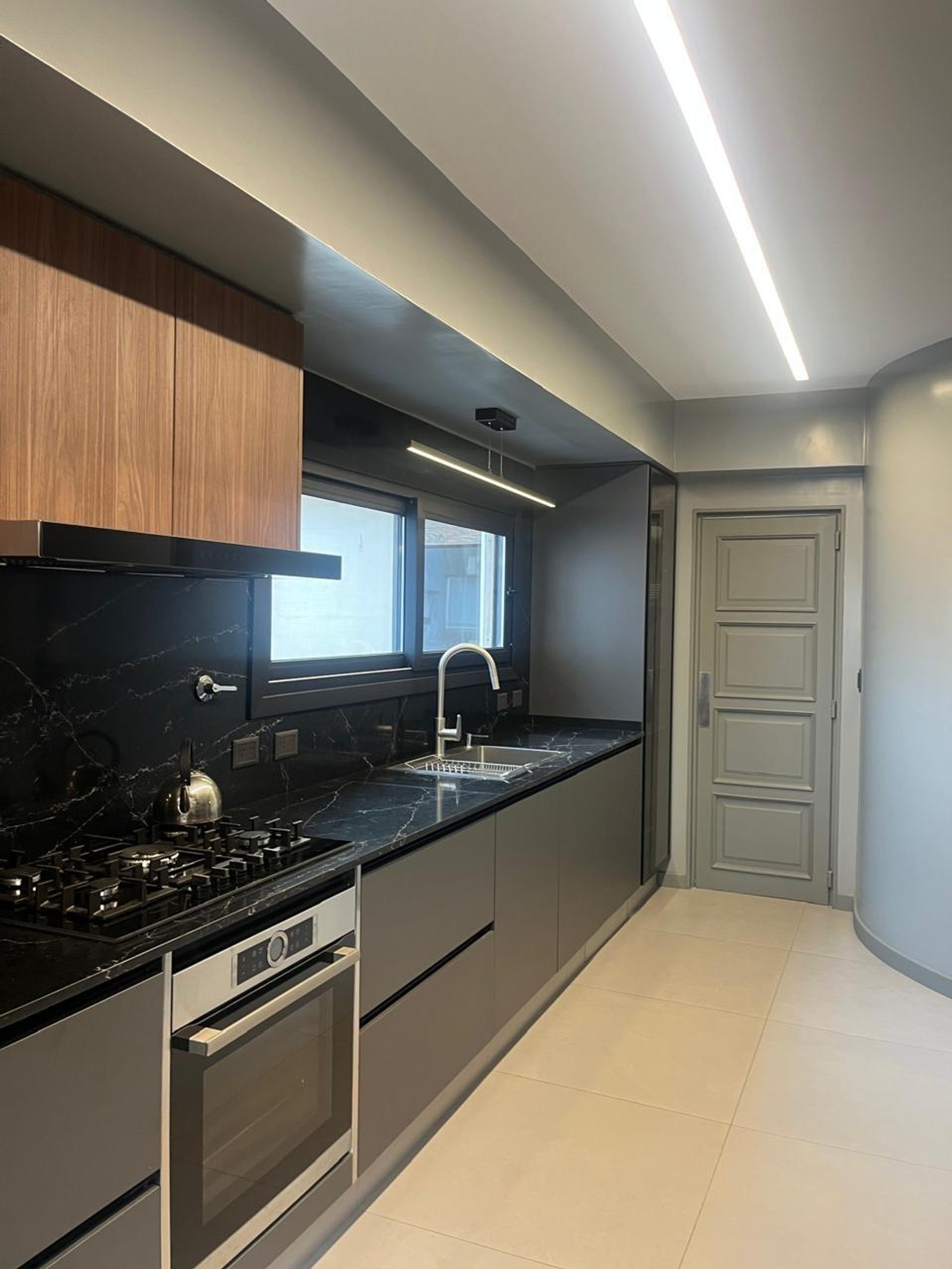 Cozinha moderna com bancada de pedra escura e armários cinza e madeira — projeto 11 de Septiembre, por cromo., em Belgrano
